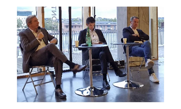 Table ronde : trois intervenants échangent au micro dans une salle vitrée donnant sur les quais